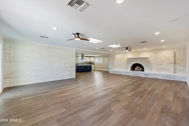 unfurnished living room with ceiling fan, a fireplace, a skylight, and dark hardwood / wood-style floors