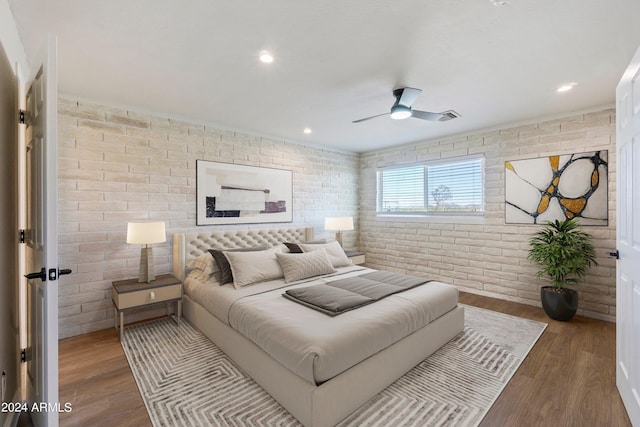 bedroom with ceiling fan, hardwood / wood-style flooring, and brick wall