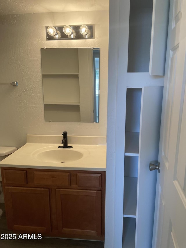 bathroom featuring vanity, toilet, and a textured wall
