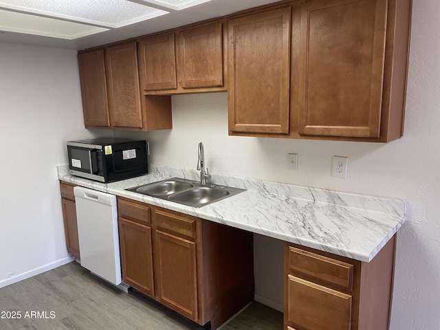 kitchen with white dishwasher, a sink, light wood finished floors, light countertops, and brown cabinetry
