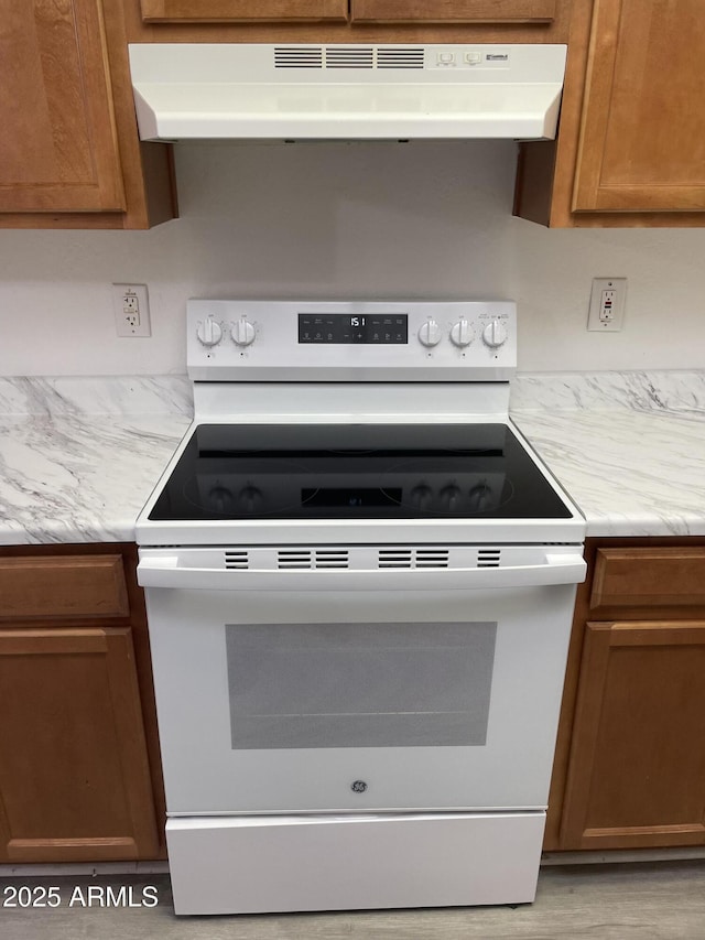 kitchen featuring white range with electric stovetop, under cabinet range hood, brown cabinets, and light wood-style flooring