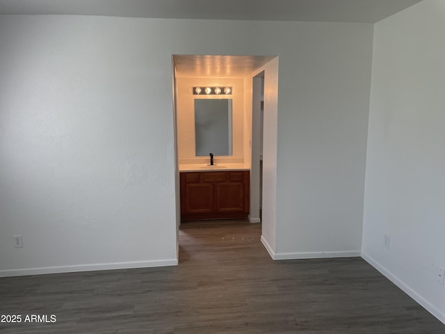 unfurnished room with a sink, dark wood finished floors, and baseboards