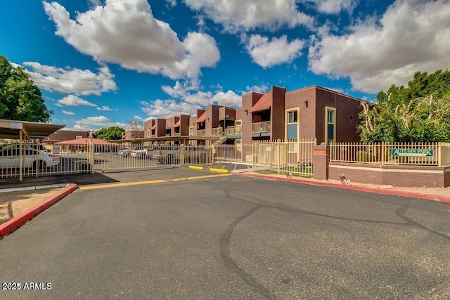 view of building exterior featuring covered and uncovered parking, fence, and a residential view