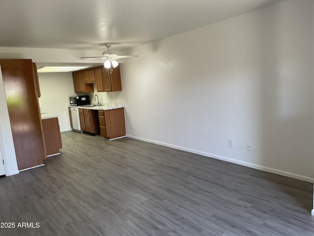 kitchen featuring ceiling fan, a sink, light countertops, dark wood finished floors, and baseboards