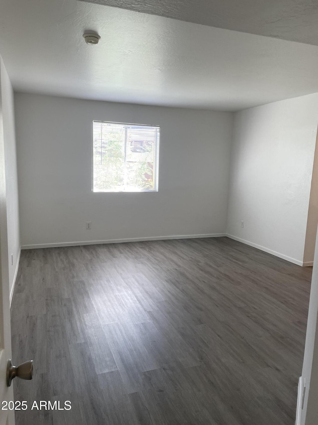 unfurnished room featuring dark wood-style flooring, baseboards, and a smoke detector