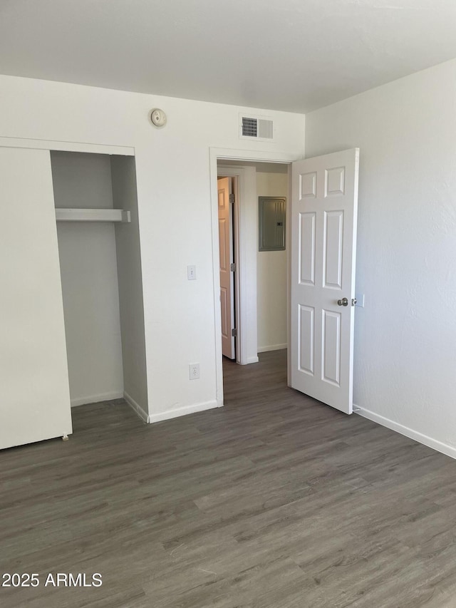 unfurnished bedroom featuring baseboards, wood finished floors, a closet, and electric panel