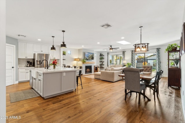 kitchen featuring decorative light fixtures, white cabinetry, an island with sink, sink, and stainless steel fridge with ice dispenser