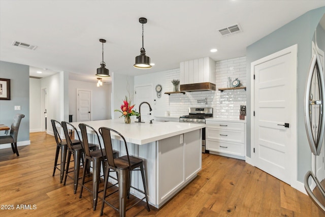 kitchen with pendant lighting, sink, white cabinetry, stainless steel appliances, and an island with sink