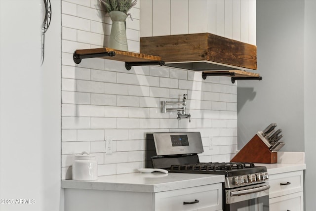 kitchen with light stone counters, decorative backsplash, stainless steel range with gas stovetop, and white cabinets