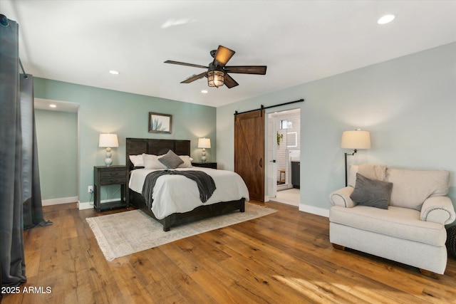 bedroom with ensuite bathroom, a barn door, hardwood / wood-style floors, and ceiling fan