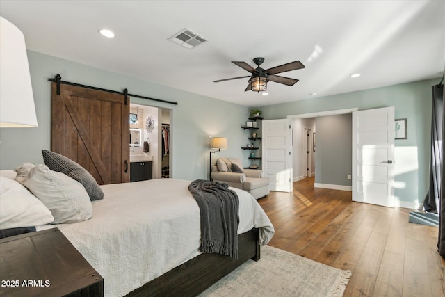 bedroom with ceiling fan, wood-type flooring, a barn door, and a spacious closet