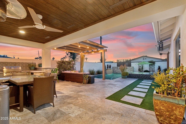 patio terrace at dusk featuring ceiling fan, an outdoor kitchen, an outdoor hangout area, and area for grilling