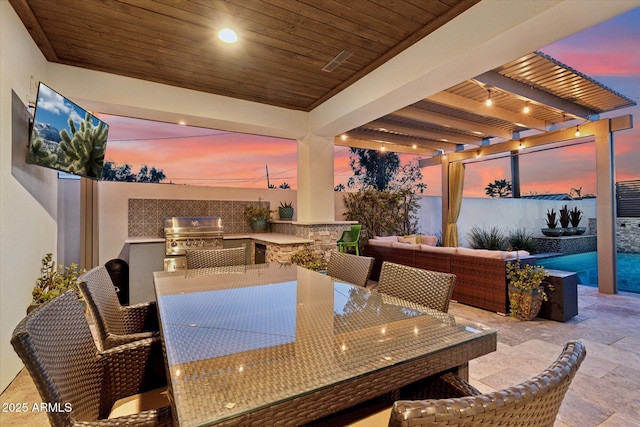 patio terrace at dusk featuring a grill, a pergola, outdoor lounge area, and exterior kitchen