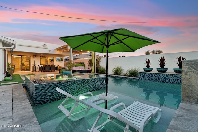 pool at dusk with outdoor lounge area and a patio area