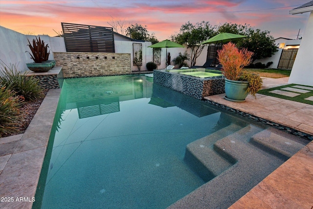 pool at dusk with an in ground hot tub