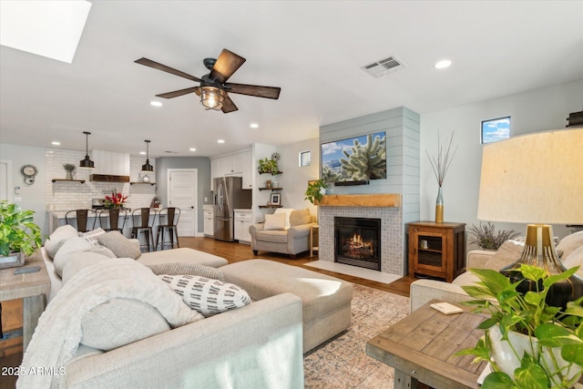 living room with ceiling fan, a skylight, and light hardwood / wood-style flooring