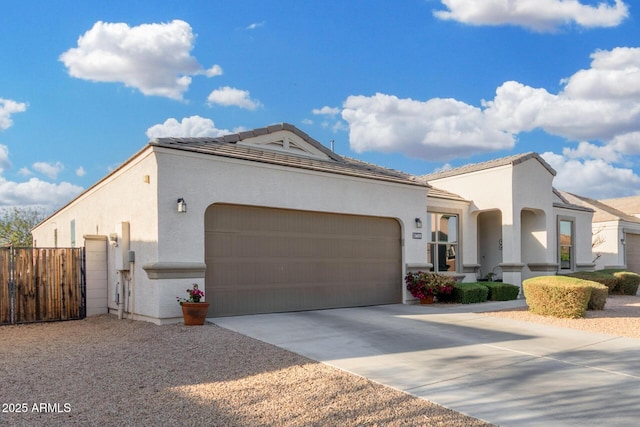 mediterranean / spanish house featuring an attached garage, fence, a tile roof, concrete driveway, and stucco siding