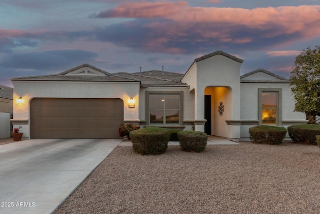 view of front of property with an attached garage, a tiled roof, concrete driveway, and stucco siding