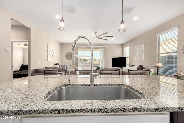 kitchen featuring open floor plan, hanging light fixtures, light stone counters, and a ceiling fan