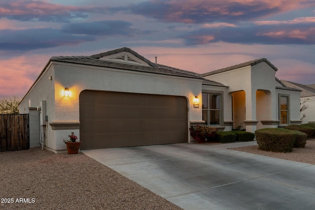 mediterranean / spanish-style house with a garage, driveway, a tile roof, fence, and stucco siding