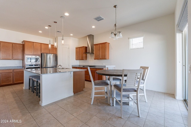 kitchen with wall chimney exhaust hood, decorative light fixtures, a kitchen island with sink, and appliances with stainless steel finishes