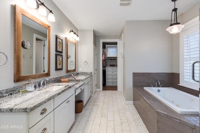 full bath featuring a walk in closet, visible vents, vanity, wood finished floors, and a whirlpool tub