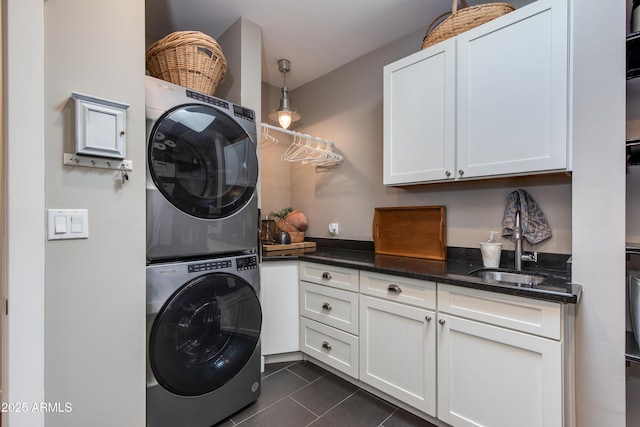 laundry room featuring a sink, cabinet space, dark tile patterned floors, and stacked washer / drying machine