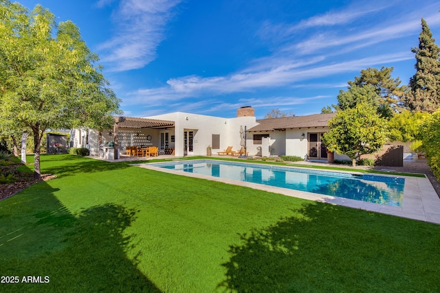 back of property with a chimney, stucco siding, a lawn, a patio area, and an outdoor pool