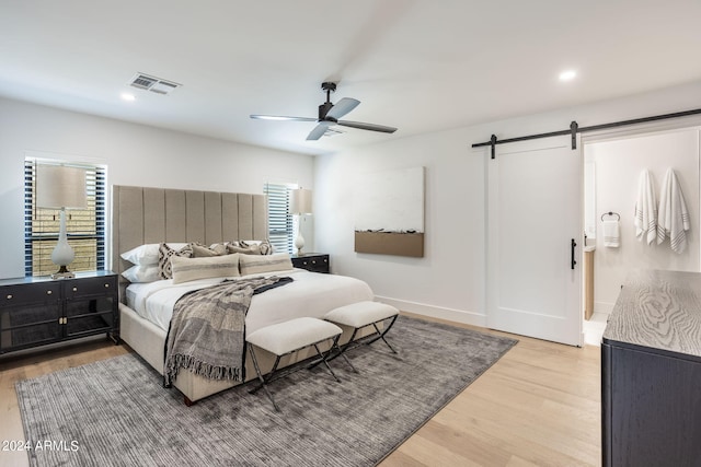 bedroom featuring light wood finished floors, a barn door, visible vents, and recessed lighting