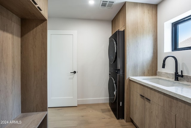 laundry area featuring stacked washer and dryer, cabinet space, visible vents, light wood-style floors, and a sink