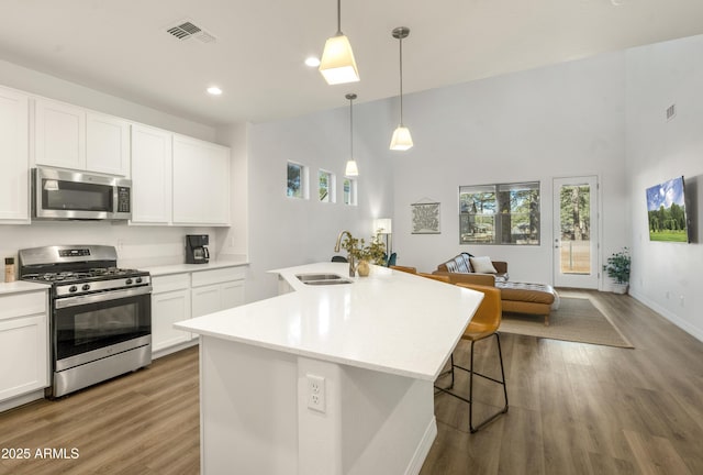 kitchen featuring an island with sink, decorative light fixtures, sink, appliances with stainless steel finishes, and white cabinets