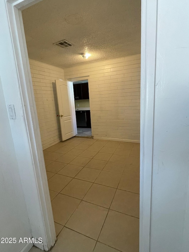 hallway featuring brick wall, a textured ceiling, and light tile patterned floors