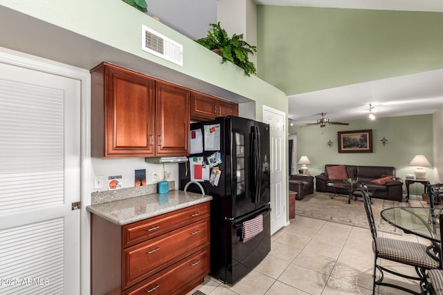 kitchen featuring light tile patterned flooring, black refrigerator, ceiling fan, and a towering ceiling