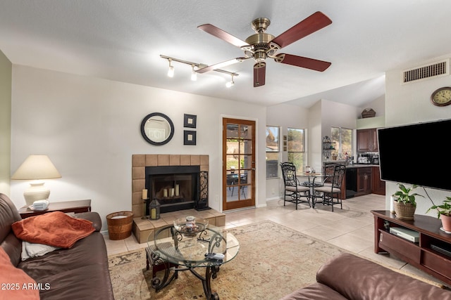 tiled living room with a tiled fireplace, vaulted ceiling, a textured ceiling, and ceiling fan