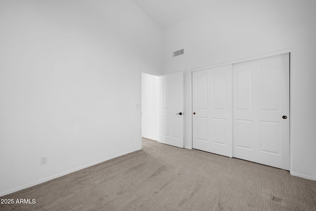 unfurnished bedroom featuring light carpet, high vaulted ceiling, and a closet