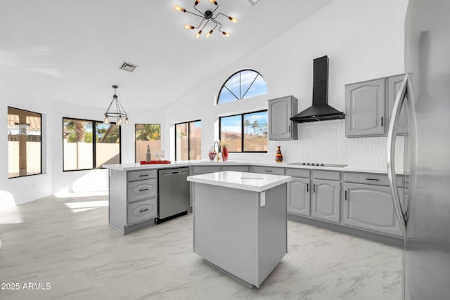 kitchen with wall chimney exhaust hood, hanging light fixtures, gray cabinets, a kitchen island, and stainless steel appliances