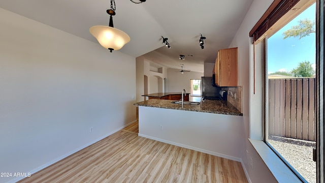 kitchen featuring sink, tasteful backsplash, decorative light fixtures, kitchen peninsula, and light wood-type flooring