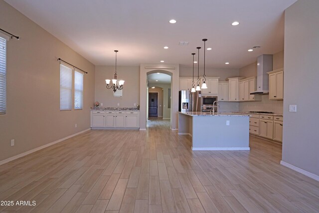 2811 S Jeffry St, Gilbert, AZ 85295 - kitchen featuring wall chimney exhaust hood, arched walkways, a chandelier, light wood-style floors, and stainless steel appliances