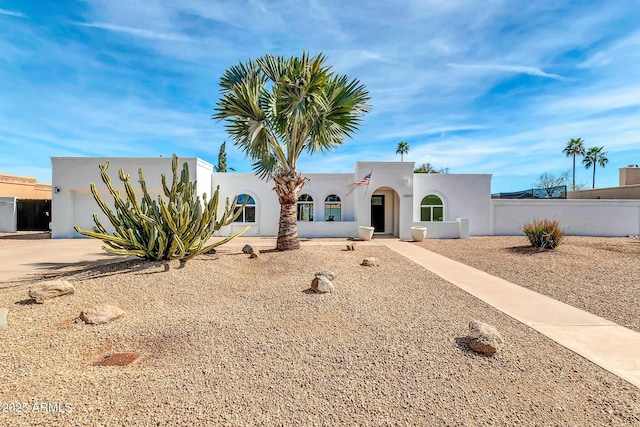 pueblo-style home featuring concrete driveway, fence, an attached garage, and stucco siding