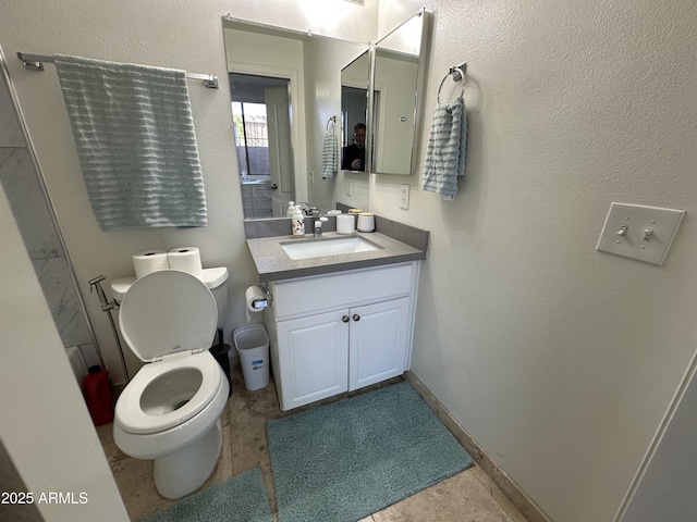 bathroom featuring baseboards, toilet, vanity, and a textured wall