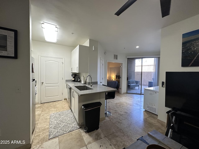 kitchen featuring visible vents, dishwasher, a kitchen bar, white cabinets, and a sink