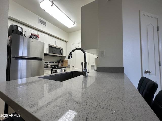 kitchen with light stone counters, a peninsula, a sink, appliances with stainless steel finishes, and white cabinetry