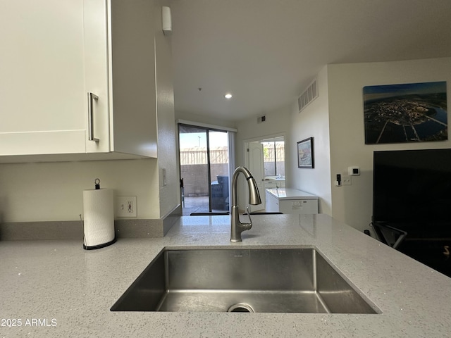 kitchen featuring visible vents, white cabinets, light stone countertops, and a sink