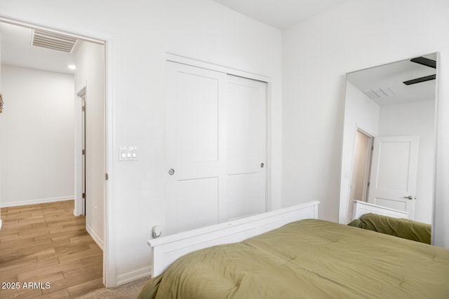 bedroom with a closet, visible vents, light wood-style flooring, and baseboards