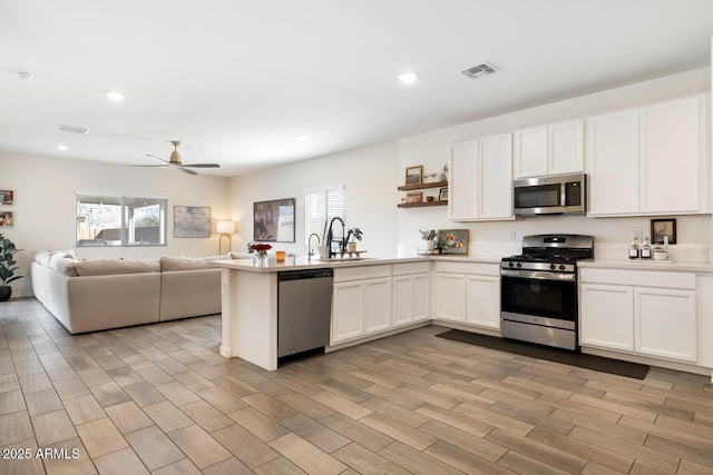 kitchen with visible vents, a sink, open floor plan, a peninsula, and appliances with stainless steel finishes