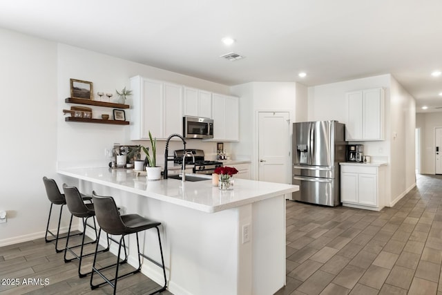 kitchen with wood finish floors, a breakfast bar, open shelves, appliances with stainless steel finishes, and a peninsula