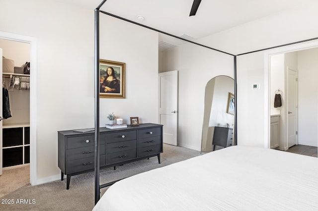 bedroom with arched walkways, a spacious closet, a closet, light colored carpet, and connected bathroom