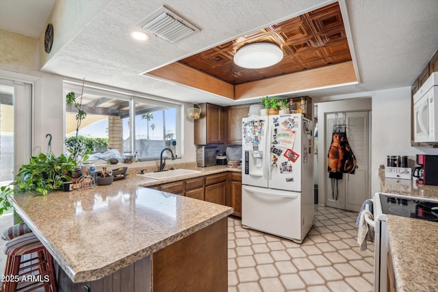 kitchen featuring white appliances, a sink, a tray ceiling, a peninsula, and light countertops