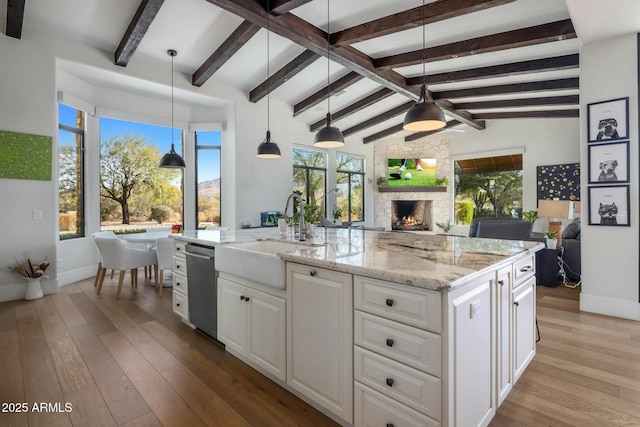 kitchen with a sink, a fireplace, open floor plan, white cabinets, and vaulted ceiling with beams