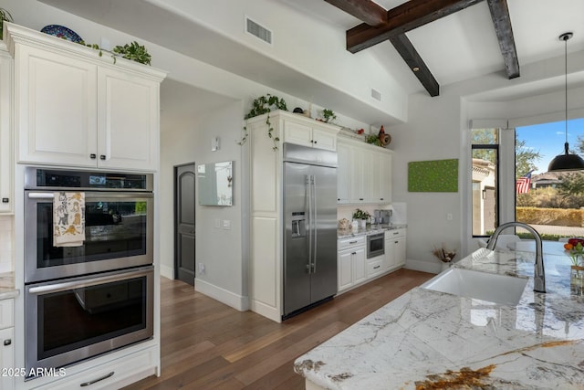 kitchen with light stone counters, white cabinets, beamed ceiling, stainless steel appliances, and a sink